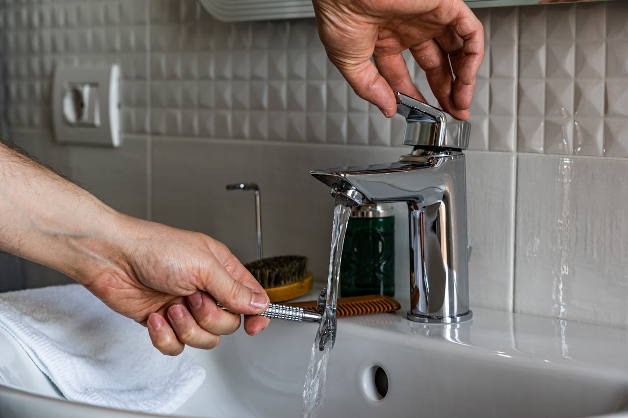 our-experience Close-up image of a man washing a shaver under a bathroom faucet, emphasizing cleanliness.