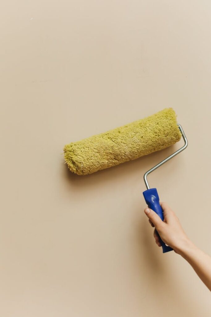 pexels-photo-5583124 Hand holding a paint roller applying fresh coat on beige wall in home improvement project.